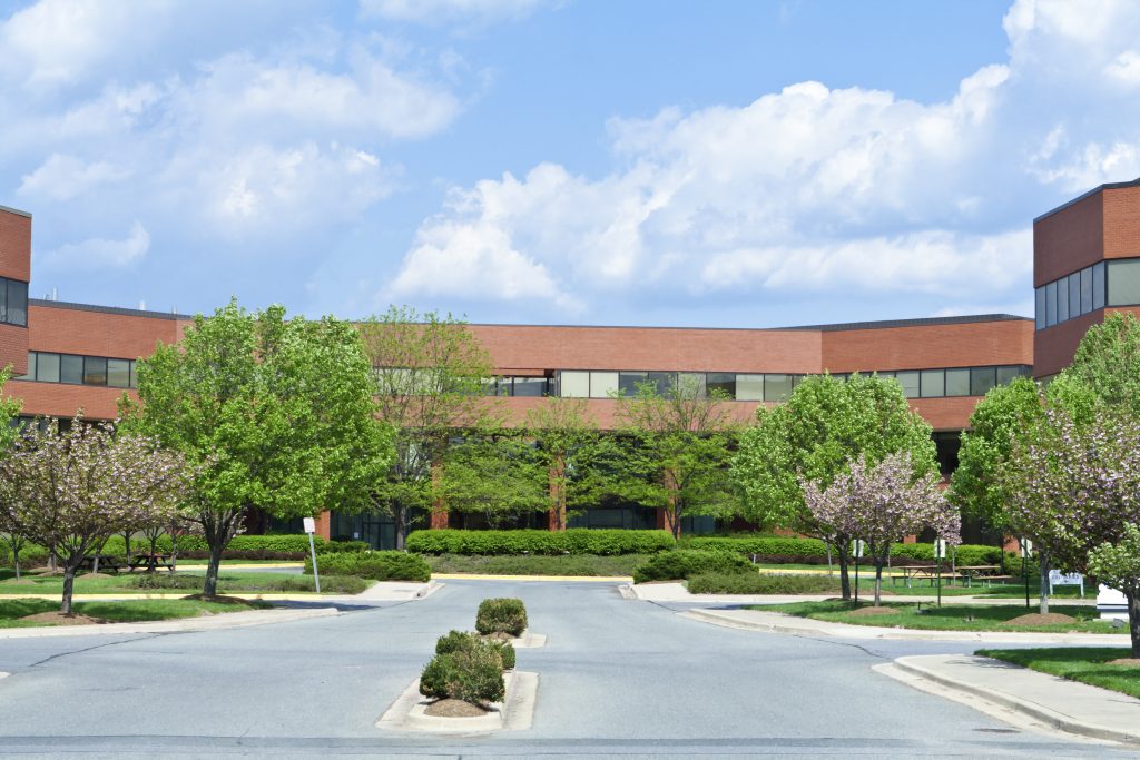 Sprawling red brick office building in suburban Maryland, United States. Building is set back from the road, and has low trees in front.